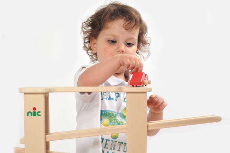 Półtoraroczny chłopiec bawi się kulodromem – widoczny jest fragment drewnianej konstrukcji – zjeżdżalnia dla kulek i samochodzików.